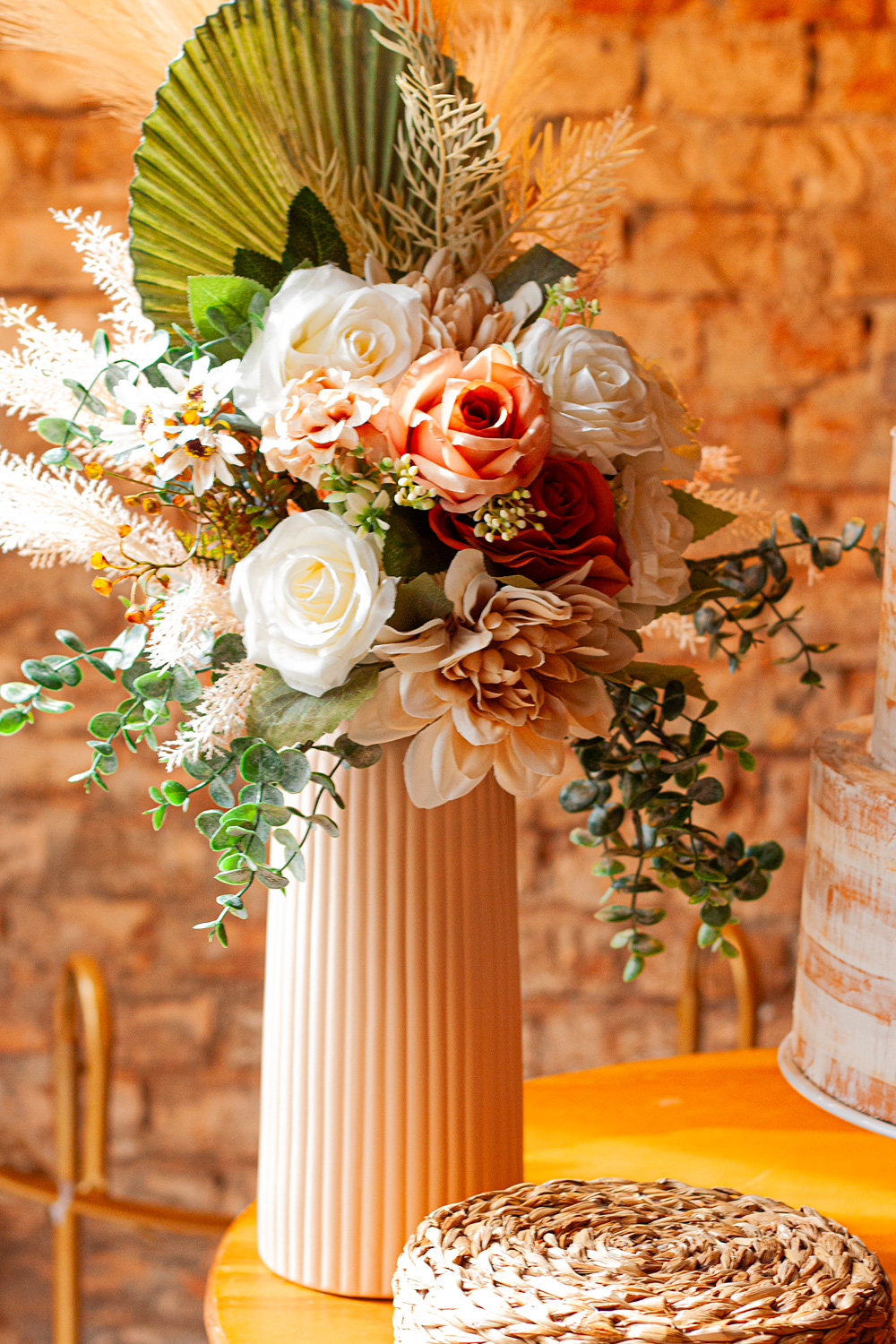 Arranjo de flores desconstruído e assimétrico para casamento intimista, com flores em tons quentes de terracota, rosa chá e branco, misturadas a folhagens verdes e texturas rústicas.